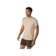 En mand står på en hvid baggrund iført en Asics Road Seamless SS Top, Herre, Cream. Han ser lidt til venstre med afslappede arme, hvilket fremhæver den åndbare åndbar træningstrøje, der er designet til hverdagskomfort.