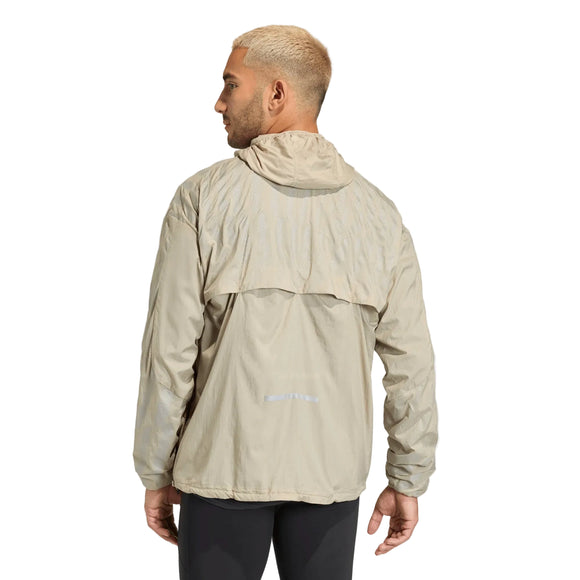 En person med kort, lysblondt hår ses bagfra iført en Adidas Adi365 High-Vis Jacket, Herre, Woca i lys beige og sorte bukser på en ensfarvet lysegrå baggrund.
