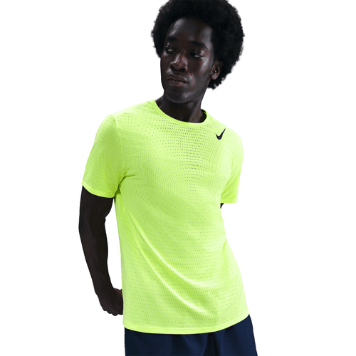 En mand bærer Nike Dri-FIT ADV Short-Sleeve Running Top til mænd i Volt/Black med perforerede detaljer, mens han står på en almindelig hvid baggrund og kigger lidt til siden.
