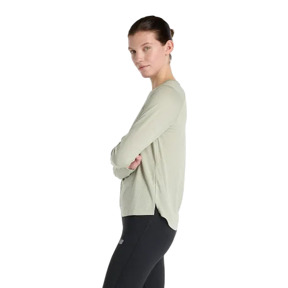 En kvinde med lys hud og tilbagestrøget brunt hår står i profil med korslagte arme iført New Balance Athletics Long Sleeve for Dame i Garter Snake Heather og sorte leggings på en almindelig hvid baggrund.