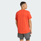 En person bærer den knaldorange Adi365 Running Tee, Herre, Duor fra Adidas med grå shorts og kigger væk for at vise bagsiden af denne adidas løbetrøje - ideel til løbetræning - mod en almindelig lys baggrund.