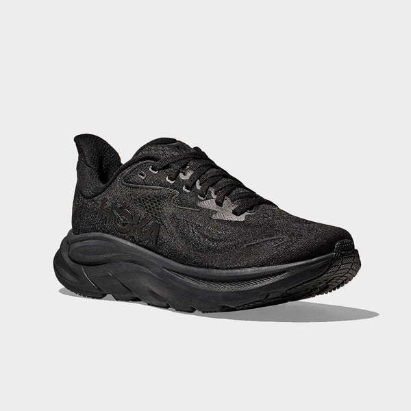 Hoka Clifton 10 Herre i sort/sort har en tyk støddæmpende sål, åndbar mesh-overdel og Hoka-mærke på siden. Skoen vises i en vinkel mod en almindelig grå baggrund.
