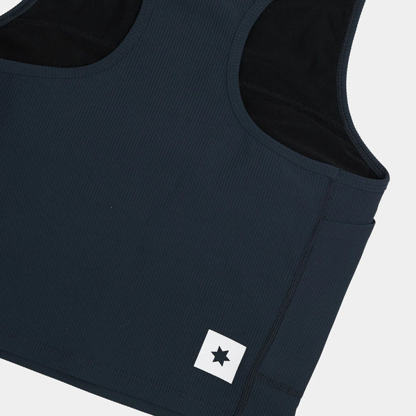 Nærbillede af Saysky W Combat Rib Crop Top til kvinder i blå, tankmodel med ribbet struktur og et hvidt rektangulært mærke med en sort stjerne nederst til venstre foran på en almindelig lys baggrund.
