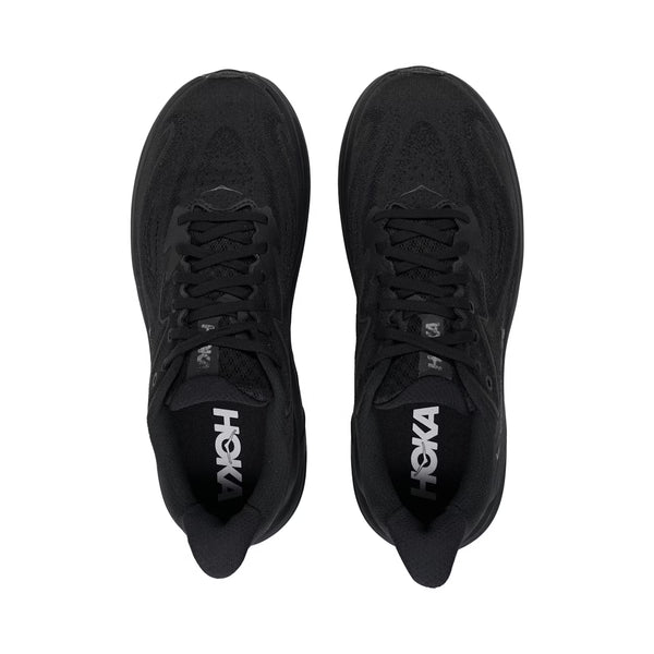 Et par Hoka Clifton 10, Dame, Black/Black løbesko med sorte snørebånd er vist ovenfra på en hvid baggrund. HOKA-logoet ses på indlægssålerne - perfekt som komfortable løbesko til damer.