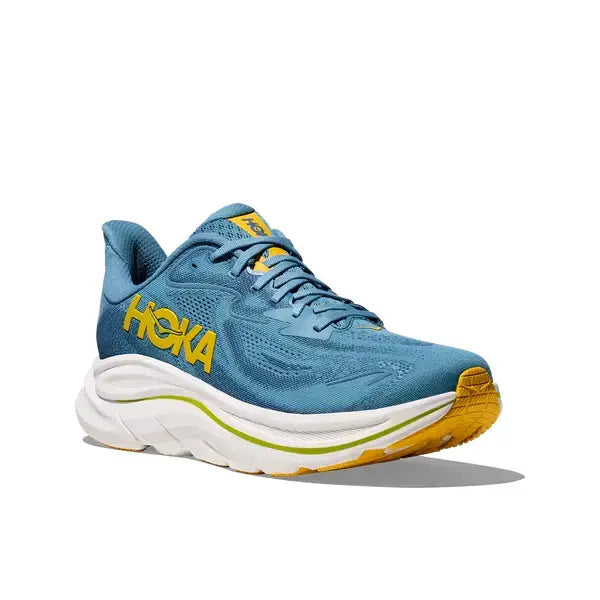 Clifton 10 Herre fra Hoka i Alpine Blue/Foggy Night har gule detaljer og branding, en hvid polstret sål og er vist på en almindelig hvid baggrund.
