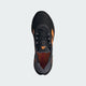 Adidas Adistar Byd Herre løbesko i Cblack/Luor/Auon er vist ovenfra med orange accenter og Adidas-logoet på tungen, sat mod en almindelig lysegrå baggrund.