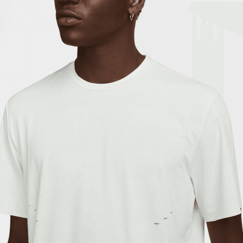 En person er iført en Nike Dri-FIT ADV kortærmet løbetop, Herre, i Summit White/Blkref. Billedet viser det øverste af brystet, skuldrene og det nederste af ansigtet. Vedkommende har også en lille ørering.