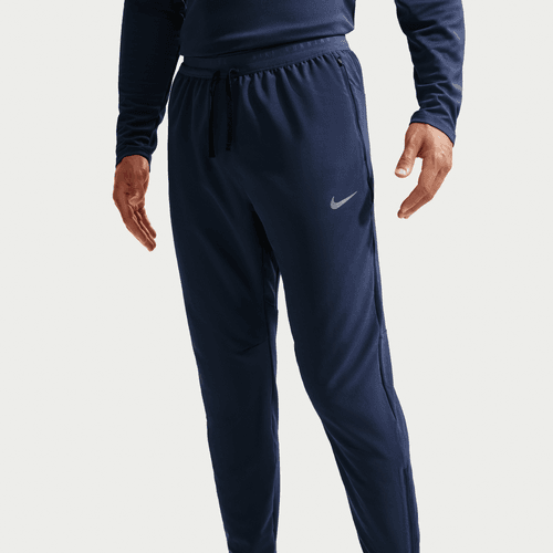En person står iført Nike Stride Woven Running Pants, Herre, i Midnight Navy/Reflective Silv og en matchende langærmet top. Kun kroppen fra skuldrene og ned er synlig. Bukserne har åndbart materiale, snøre i taljen og et Nike-logo på venstre lår.