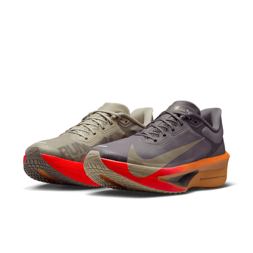 Et par Nike Zoom Fly 6 Herre i Desert Khaki/Cave Stone-Monarch med uensartede farver: venstre sko beige med sort sål, højre sko grå med orangerød sål, begge med den ikoniske Nike-swoosh.