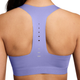 Der ses et billede af en person set bagfra, der bærer Nike High-Support Lightly Lined Sports Bra til kvinder i farven Purple Pulse. BH’en har et racerback-design med en lodret række af små ventilationshuller ned ad midten. Personens skuldre og øvre ryg er synlige, hvilket understreger, at denne sports-BH er ideel til løbetræning.