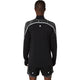 En person kigger væk fra kameraet iført en Asics Limited Series Lite-Show LS Top til mænd i Performance Black med reflekterende detaljer på skuldrene og sorte shorts med hvid kant.