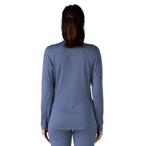 En person med langt brunt hår i hestehale ses bagfra iført en Patagonia Cap TW Zip Neck, Dame, Current Blue-top og matchende blå bukser på en almindelig hvid baggrund.