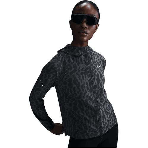 En person iført store mørke solbriller og en sort Nike Dri-FIT løbejakke til kvinder i Black/Anthracite/Reflective Silver med hætte står på en hvid baggrund og poserer afslappet med den ene hånd på hoften.