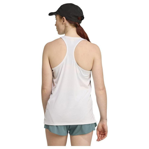 En kvinde iført Adizero Archive Running Singlet til damer i hvid/preloved teal, teal shorts og en sort kasket står med ryggen og sin hestehale synlig mod en ensfarvet hvid baggrund.