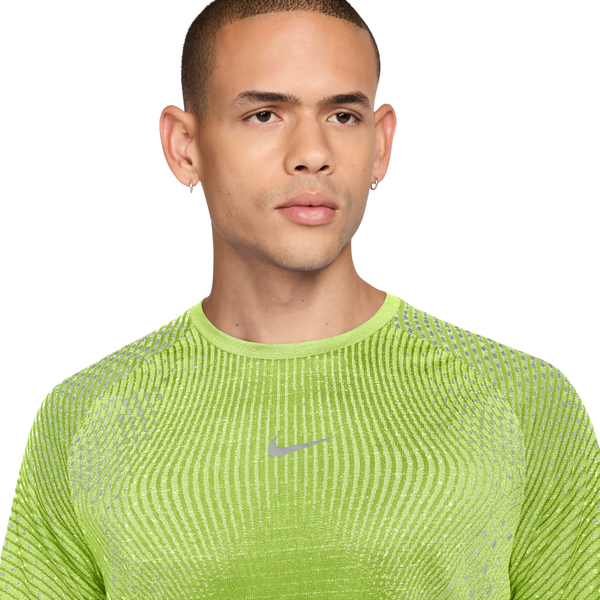 En mand har en limegrøn Nike Stride Aero-FIT løbetrøje med korte ærmer på, Herre, Lt Lemon Twist/Reflective Silver, der er fremstillet af et struktureret stof og har et reflekterende logo på brystet.