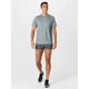 En mand iført en lysegrå atletisk T-shirt, New Balance RC Ultra Light Split Short 3" i Urgent Red og sorte løbesko går fremad mod en almindelig hvid baggrund.