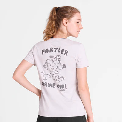 En kvinde med lysebrunt hår i hestehale står med ryggen til kameraet iført den hvide Saysky W Statement Pace T-shirt til kvinder med en tegnet yeti og teksten "Fartlek Game On!" på ryggen.