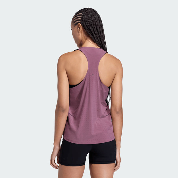 En person med flettet hår ses bagfra, iført en rødbrun Adidas Adi365 Hk Singlet Dame Shafig og sorte shorts, stående mod en almindelig lys baggrund.