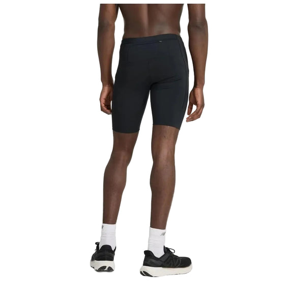 En person kigger væk fra kameraet iført New Balance NB Sleek Pocket Half Tight 9" Herre i sort sammen med hvide strømper og sorte sneakers på en almindelig lys baggrund.