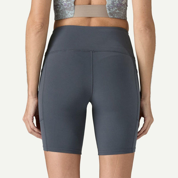 En kvinde ses bagfra iført en grå sports-bh og Patagonia W's Maipo Shorts - 8 in., Dame, Smolder Blue. Det højtaljede design i strækbart materiale giver komfort til træningsshorts kvinder; hendes arme er afslappede i siderne.
