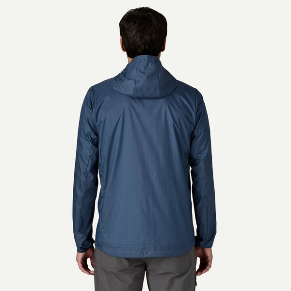 En person ses bagfra iført Patagonia Houdini Jkt, Herre, Clement Blue - en ultralet vindjakkeideel som herre løbejakke - sammen med grå bukser på en almindelig lys baggrund.