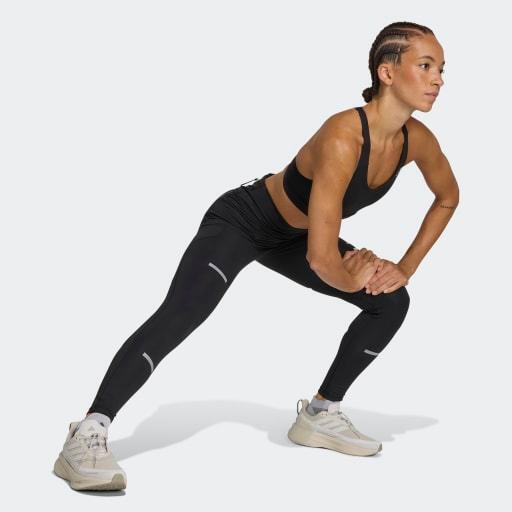 En kvinde i sportstøj og Adidas Adi365 Leggins, Dame, Black udfører en sidelæns udstrækning mod en almindelig lys baggrund.