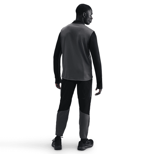 En mand kigger væk fra kameraet og er iført en Nike Pacer Winterized 1/2-Zip Running Top i Anthracite/Black/Reflective Silver med matchende bukser og sorte sko. Tøjet har mørke- og lysegrå paneler mod en almindelig hvid baggrund.
