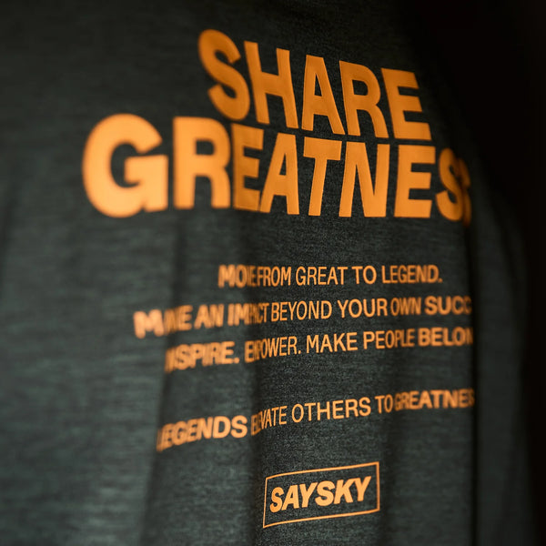 Den grønne Statement Pace Long Sleeve til herrer fra Saysky har fed orange SHARE GREATNESS-tekst, mindre inspirerende sætninger og et Saysky-logo i et rektangel nær kanten. Svedtransporterende for ultimativ komfort.