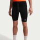 En person iført sorte Nike ACG Lavaloops 1/2 Tights til mænd med et hvidt trekantlogo, udformet som sportsshorts, kombineret med en lys orange top og hvide sokker - perfekt træningstøj.