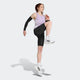 En kvinde i en svedtransporterende Adidas Adizero Singlet, Dame, Powplu/Maglil, sorte kompressionsshorts og hvide Adidas-sneakers løfter sit knæ og sin arm, mens hun laver løbeopvarmning på en ensfarvet baggrund.