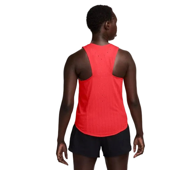 En kvinde ses bagfra iført en Nike AeroSwift Singlet, Dame, i Lt Crimson/Black/Black med sorte shorts. Racerback-toppen har små ventilationshuller og ligner en åndbar løbevest. Baggrunden er helt hvid.