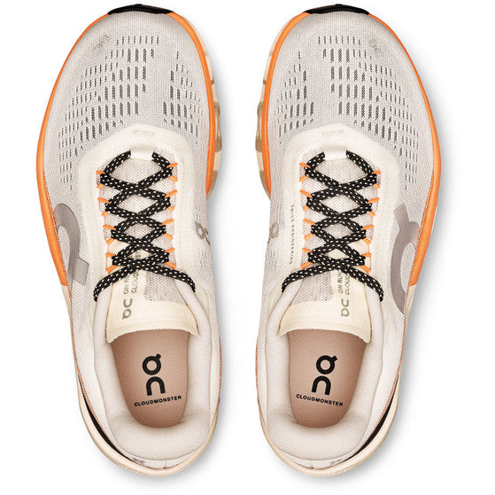 Et billede ovenfra af On Cloudmonster 2 dame løbesko i Ivory/Tangerine viser beige sko med orange detaljer, sorte og hvide snørebånd, Helion superfoam-støddæmpning og On-logoet på tungen og siden.