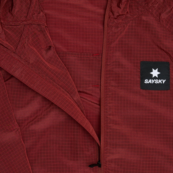 Nærbillede af Saysky Clean Pace Shield Jacket til mænd i rød med gittermønster og et sort brystmærke med en hvid stjerne og teksten "SAYSKY", delvist lynet op.