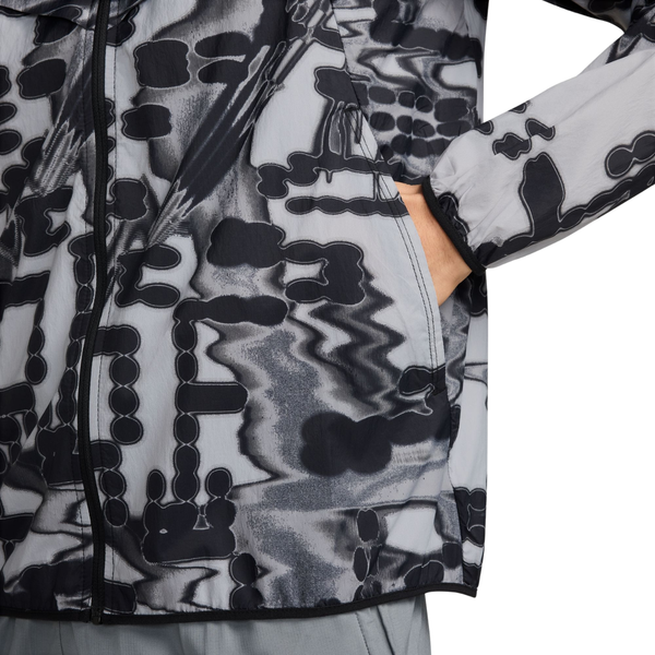 Nærbillede af en grå og sort mønstret, vandafvisende Nike Repel UV Protection løbejakke, Herre, Stealth, med en hånd i sidelommen.