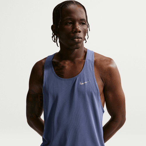 En person med flettet hår bærer en Nike Nk Df Fast Singlet til mænd i Diffused Blue/Reflective Silver, står på en almindelig hvid baggrund og kigger lidt til siden med et neutralt udtryk.