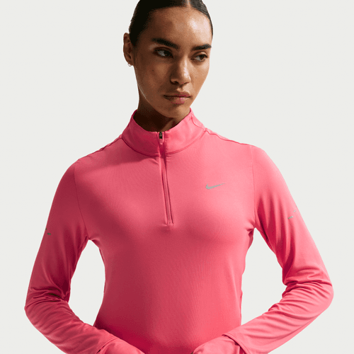 En kvinde iført Nike Swift UV Half Zip Running Top i Sea Coral/Reflective Silver med kvart lynlås og et lille Nike-logo på brystet står på en ensfarvet baggrund og kigger lidt til siden.
