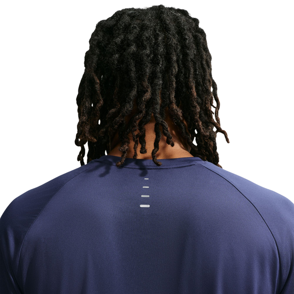 Der vises et billede bagfra af en person med lange, snoede dreadlocks, der bærer en Nike Dri-FIT ADV langærmet løbetrøje til mænd i farven Midnight Navy/Reflective Silver, med fire små reflekterende striber placeret lodret på den øverste del af ryggen. Baggrunden er hvid.
