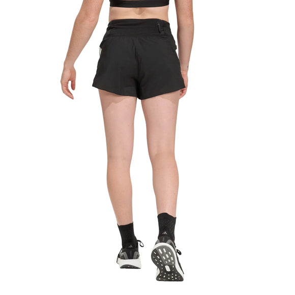 En kvinde ses bagfra iført en sort sports-bh, Adidas Adi365 Shorts, Dame, Black, sorte sokker og sorte løbesko mod en almindelig lys baggrund, der fremhæver stilen i disse træningsshorts fra Adidas.