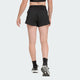 En kvinde ses bagfra iført en sort sports-bh, Adidas Adi365 Shorts, Dame, Black, sorte sokker og sorte løbesko mod en almindelig lys baggrund, der fremhæver stilen i disse træningsshorts fra Adidas.