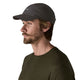 En mand med lysebrunt hår, skæg og overskæg bærer en Patagonia Ultralightweight Ridge Hat i sort og en olivengrøn t-shirt, vist i profil mod en almindelig hvid baggrund.