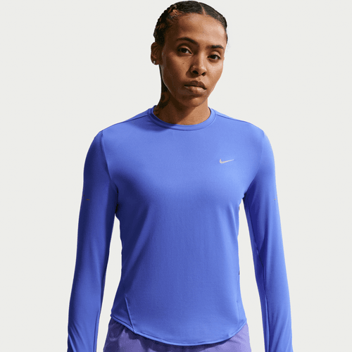 En kvinde i Nike Swift UV Long Sleeve Shirt, Dame, Sapphire/Reflective Silv og fremstillet af fugttransporterende stof står med et neutralt udtryk mod en almindelig hvid baggrund.