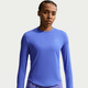 En kvinde i Nike Swift UV Long Sleeve Shirt, Dame, Sapphire/Reflective Silv og fremstillet af fugttransporterende stof står med et neutralt udtryk mod en almindelig hvid baggrund.