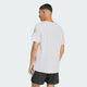 En mand kigger væk fra kameraet iført en Adidas Adi365 Running Tee, Herre, White med tre lysegrå striber på ærmet og sorte shorts med hvide striber på en almindelig lys baggrund.