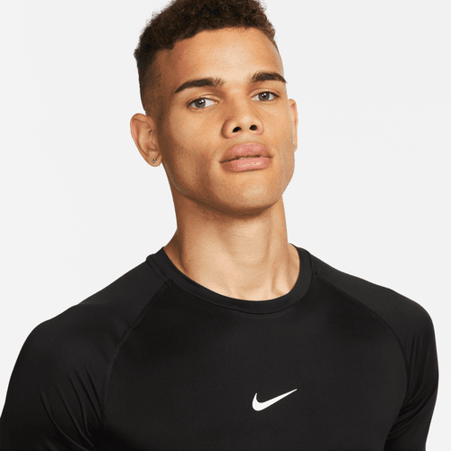 En person med kort krøllet hår bærer en sort/hvid Nike Df Tight Top Ss, herre, og ser på kameraet med et neutralt udtryk mod en almindelig hvid baggrund.