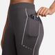 En person stikker en smartphone ned i sidelommen på Nike Therma-FIT ADV High-Waisted 7/8 Reflective Running Leggings til kvinder, der har synlige syninger og et tætsiddende design i Thunder Grey/Dk Smoke Grey.