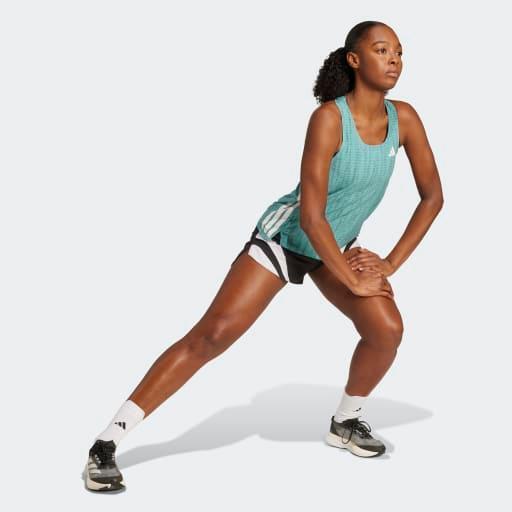 Iført en Adidas Adizero Singlet til kvinder i Powtea/Pretea udfører en person et sidelonge-stretch på en almindelig, lys baggrund.