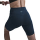 Personen strækker sig i Nike Medium-Support High-Waisted 8" Biker Shorts til kvinder, Black/Anthracite/Dk Smoke Grey, og en sort top, her set bagfra mod en almindelig hvid baggrund.