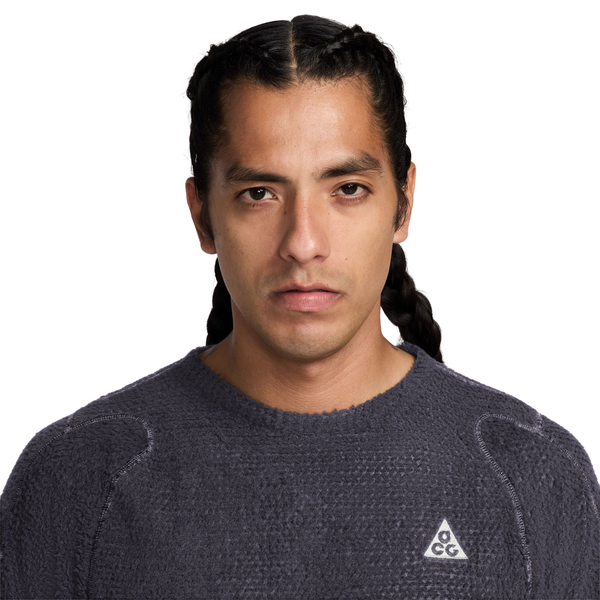 En person har en mørkegrå, langærmet Nike-trøje med rund hals og struktureret overflade på, Herre, i farvekombinationen Gridiron/Summit White, med et lille trekantet logo på brystet.