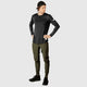 En person iført en sort langærmet skjorte, Saysky Pace Pants Herre i grøn, sorte sneakers og en bagudvendt sort kasket står på en almindelig lysegrå baggrund med hænderne på hofterne.
