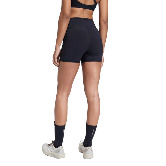 En kvinde ses bagfra iført sort sports-bh, Adidas Adi365 Hk Tight Dame i sort, sorte strømper og hvide sneakers på en almindelig lys baggrund.
